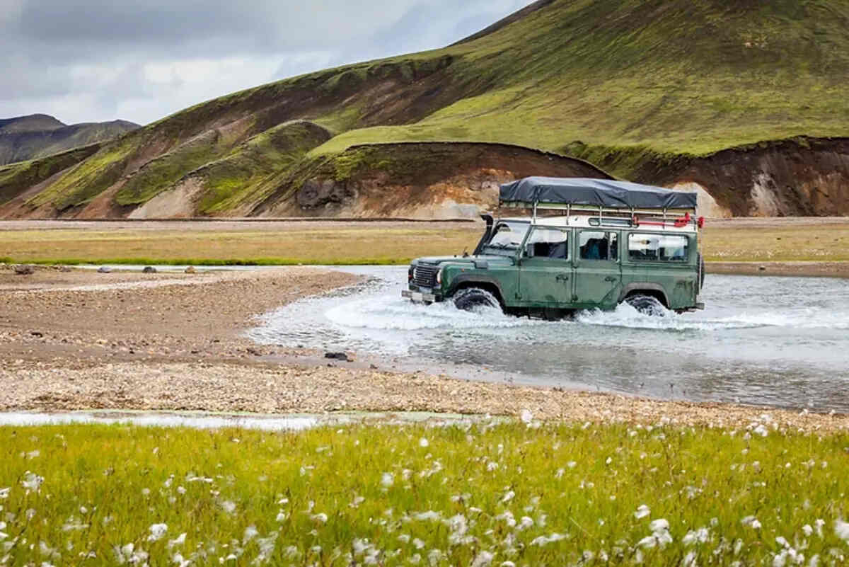 Assurances obligatoires et facultatives Un véhicule tout-terrain traverse une rivière peu profonde dans un paysage montagneux verdoyant en Islande.