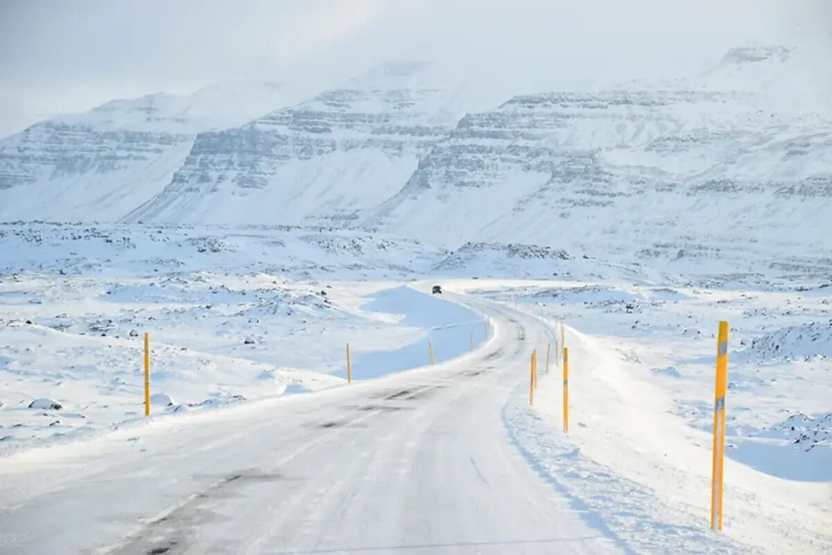 Conduire en Islande Route enneigée serpentant à travers un paysage montagneux recouvert de neige en Islande.