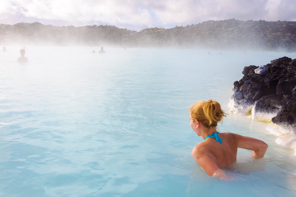Une femme se détend dans les eaux chaudes et bleu laiteux de la célèbre Blue Lagoon en Islande, entourée d'un paysage volcanique et d'une brume apaisante.