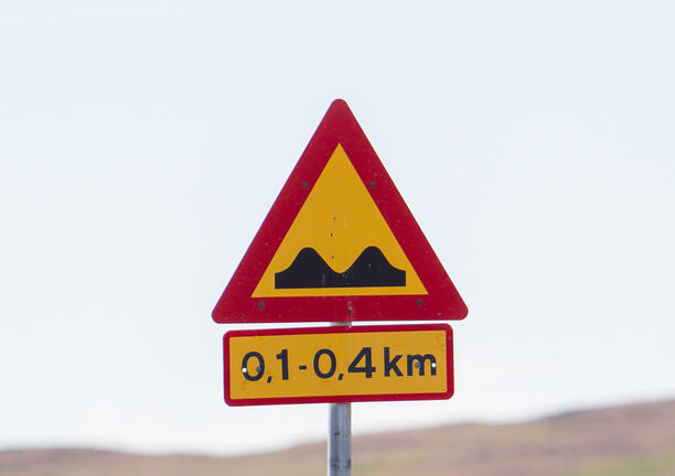 Panneau de signalisation islandais avertissant de la présence de dos d'âne sur une route rurale, entouré de champs verts et d'un horizon dégagé.
