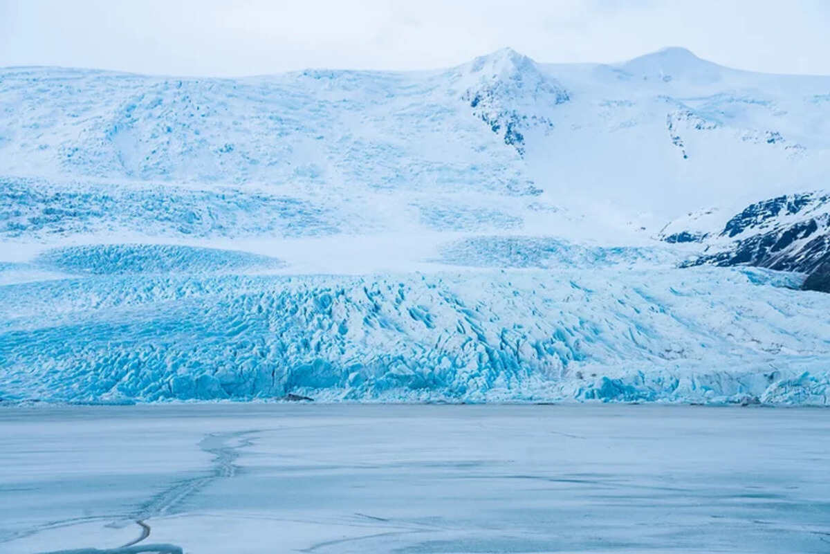 Un glacier islandais s'étend majestueusement avec des nuances de bleu glacé sous un ciel clair.