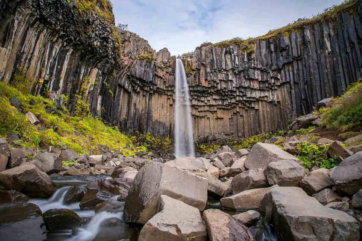 Vue emblématique de la cascade Svartifoss avec ses colonnes de basalte noires et son eau qui tombe en cascade.