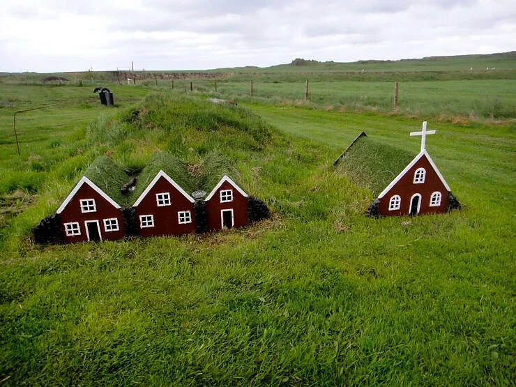 Maisons miniatures traditionnelles d'elfes en Islande, alignées avec une église miniature, intégrées dans le paysage naturel.