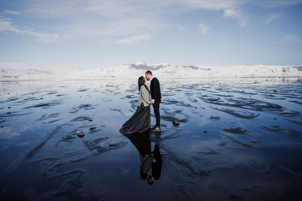 Un couple de mariés pose sur un lac gelé en Islande, créant un reflet saisissant dans un environnement hivernal féérique.