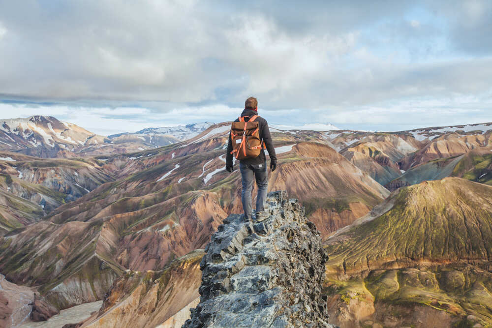 Un randonneur au sommet d'une crête rocheuse, admirant les montagnes colorées et vallonnées de Landmannalaugar, entouré par une nature sauvage à couper le souffle.
