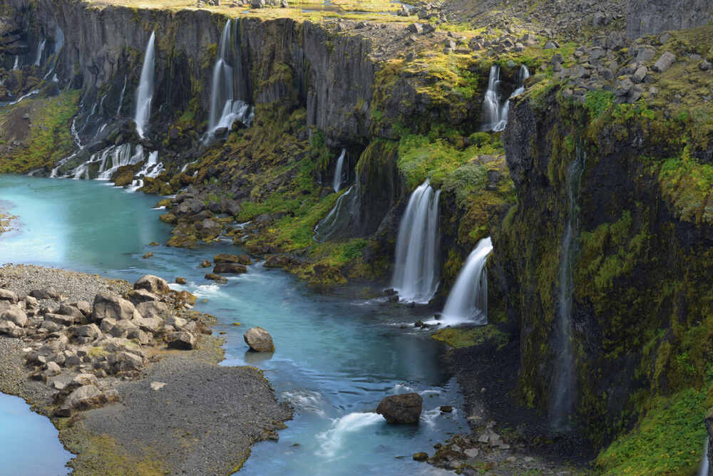 Les cascades de Sigoldugljufur dévalant des falaises couvertes de mousse, avec une eau turquoise brillante coulant paisiblement dans une vallée isolée.