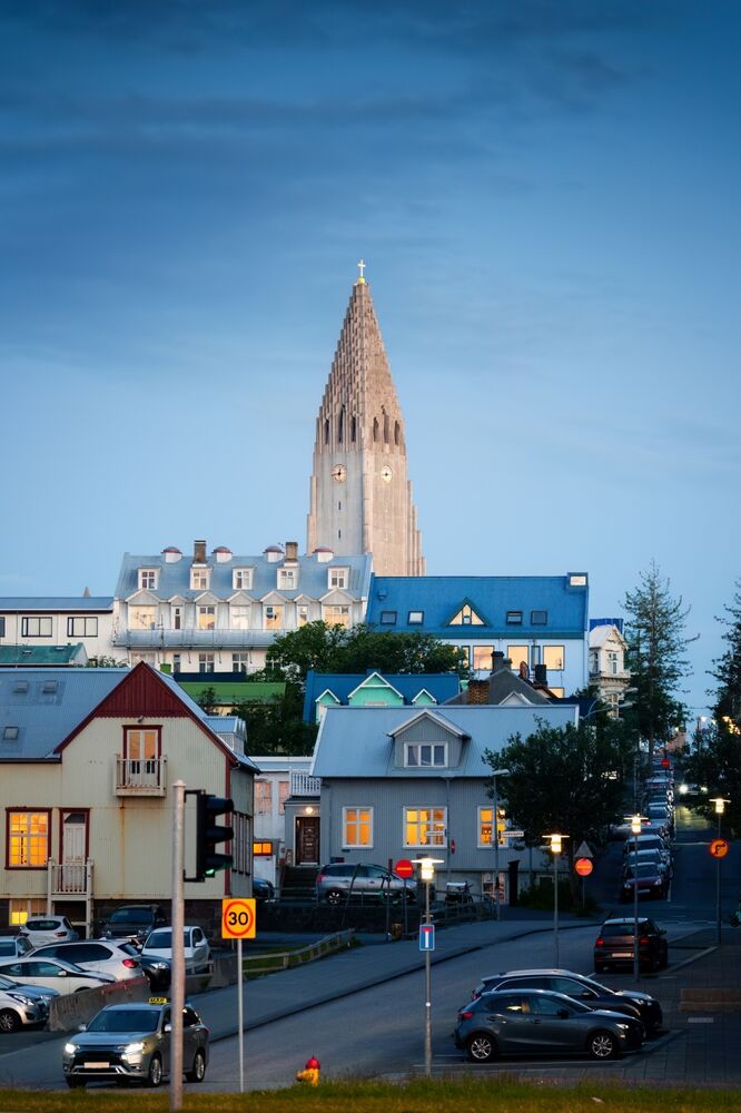 Parking gratuit au centre-ville de Reykjavik Vue du centre de Reykjavik au crépuscule, avec des maisons colorées et des voitures garées. En arrière-plan, la célèbre église Hallgrímskirkja s'élève majestueusement sous un ciel bleu.