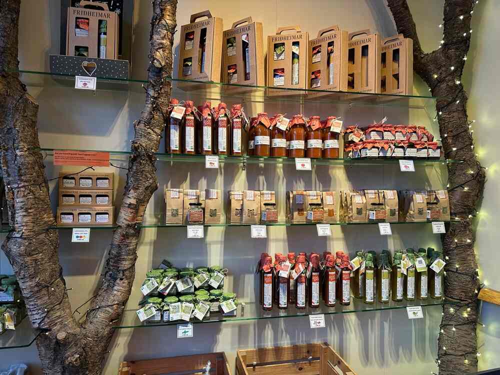 Une étagère bien organisée remplie de produits locaux islandais, y compris des bouteilles de sauces, des confitures et d'autres spécialités. L'arrière-plan est décoré avec des branches d'arbres pour une touche naturelle.