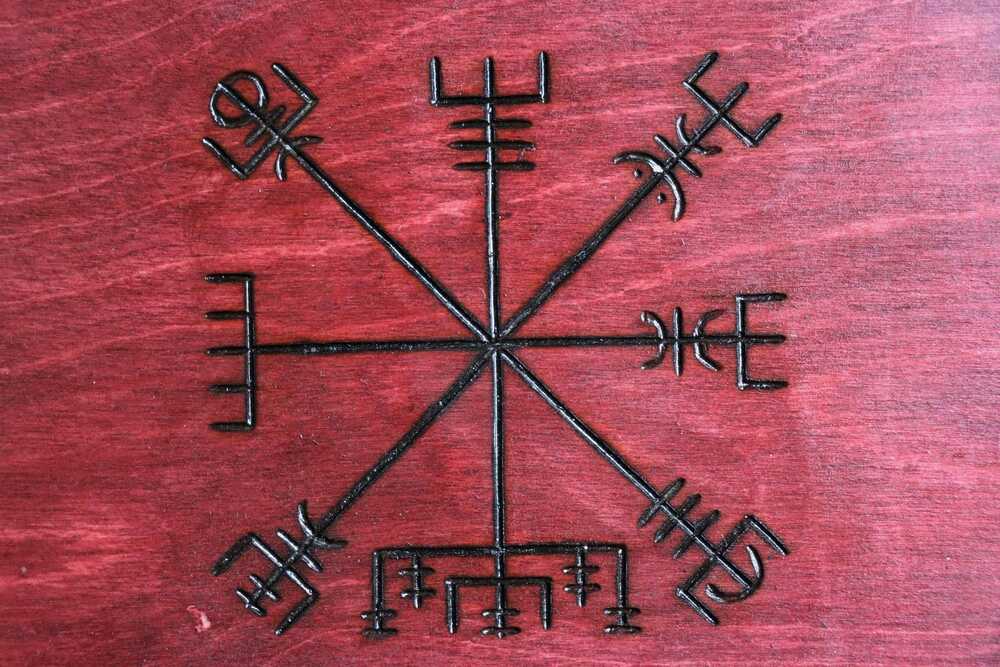 Vegvisir Représentation du symbole Aegishjalmur, également connu sous le nom de « casque de la terreur », gravé en noir sur une surface en bois rouge.