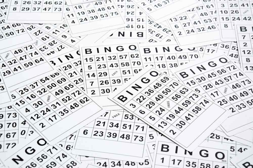 Une pile de cartons de bingo blancs remplis de numéros imprimés en noir, dispersés en désordre, donnant une impression de préparation pour un jeu amusant.