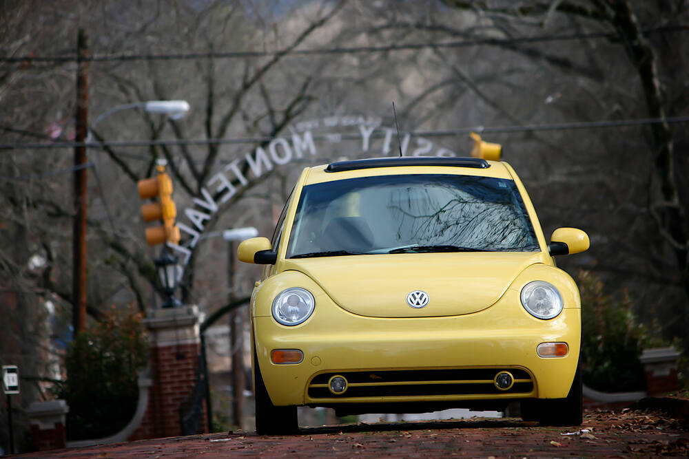 Une voiture Volkswagen Beetle jaune garée sur une rue en pente, avec l'inscription 