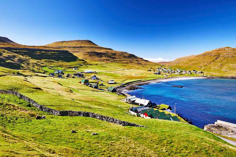 Un village côtier pittoresque entouré de collines verdoyantes. Les maisons aux toits colorés s'étendent le long du rivage, tandis que la mer d'un bleu intense contraste avec le vert des prairies.