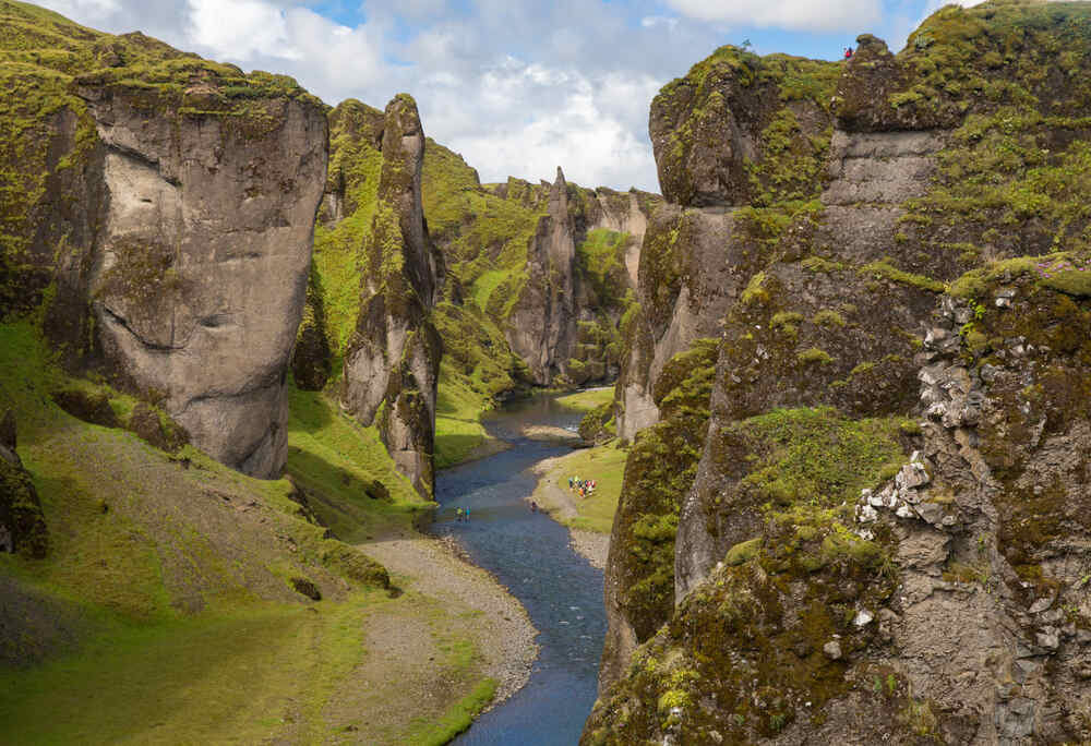 Vue spectaculaire d'un canyon islandais avec un ruisseau qui serpente au milieu des parois rocheuses verdoyantes.