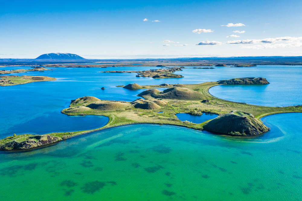 Vue aérienne du lac Mývatn avec ses petites îles volcaniques entourées d'eau turquoise et des collines verdoyantes.