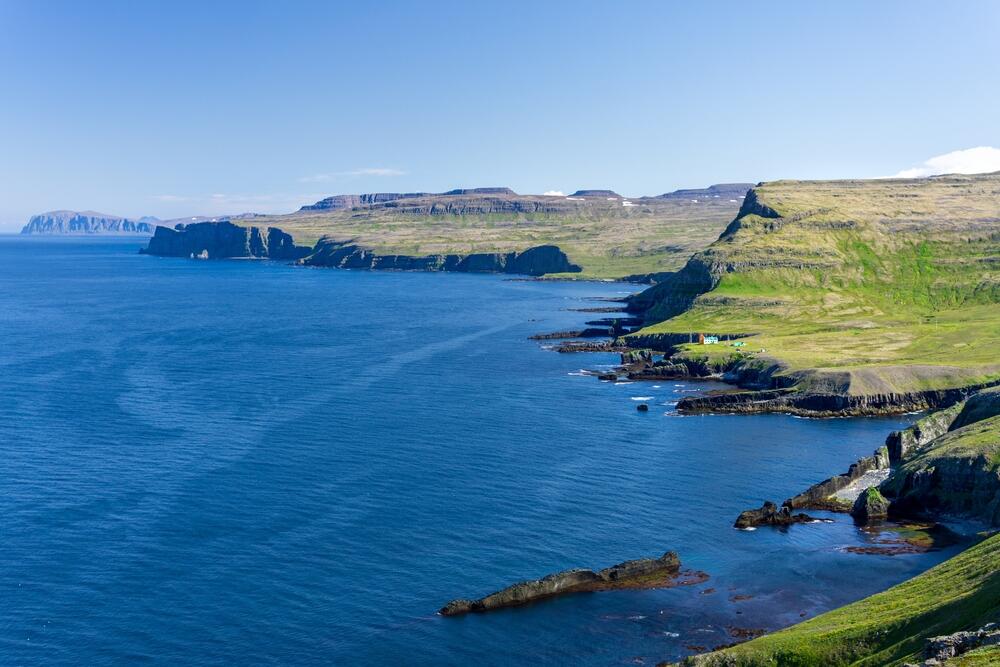 Hornstrandir - Falaises spectaculaires et nature sauvage. Vue panoramique sur les falaises verdoyantes de Hornstrandir surplombant l'océan, avec des montagnes en arrière-plan et des côtes déchiquetées.