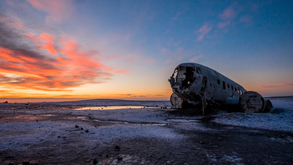 Coucher du soleil sur l'épave du DC-3 à Sólheimasandur, Islande Photo d'un épave d'avion sur la plage de Sólheimasandur en Islande, capturée au coucher du soleil avec des couleurs vives dans le ciel.
