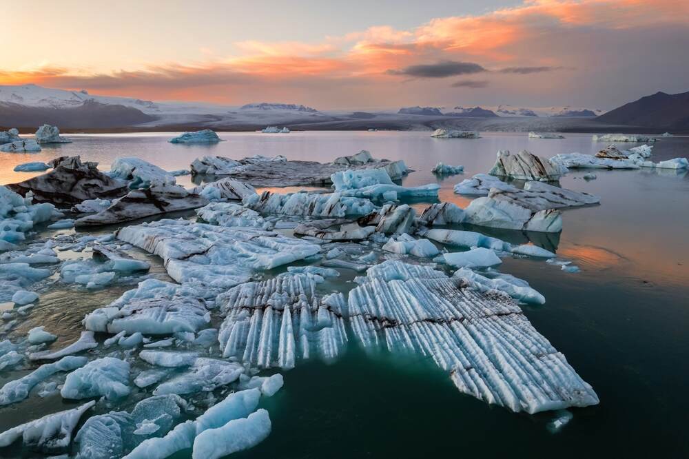 Coucher de soleil sur le lagon glaciaire Jökulsárlón en Islande avec des blocs de glace flottants sur l'eau calme.