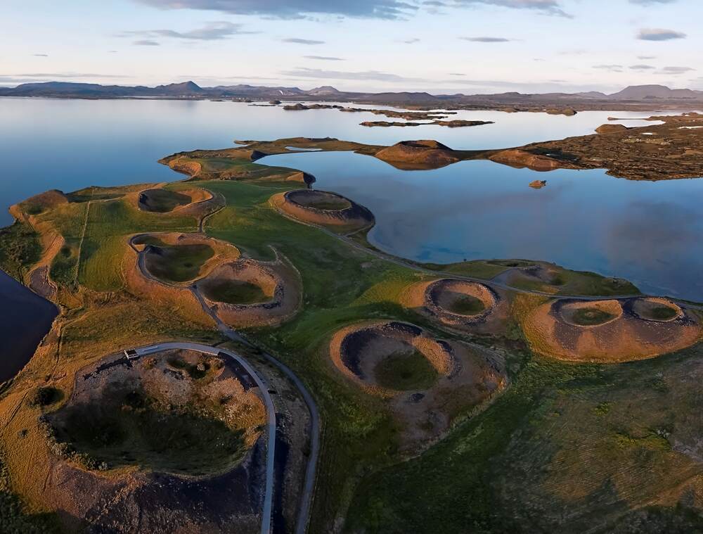 Vue aérienne du lac Mývatn entouré de formations volcaniques circulaires dans une lumière dorée du soir.