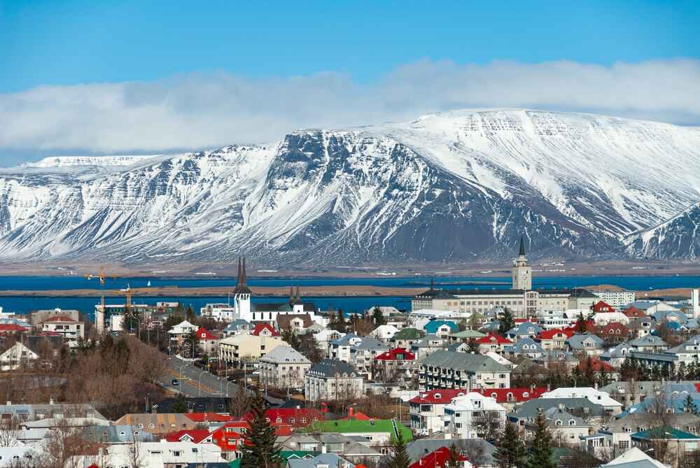 Vue panoramique de Reykjavik avec ses maisons colorées, l'église Hallgrímskirkja et les montagnes enneigées en arrière-plan.