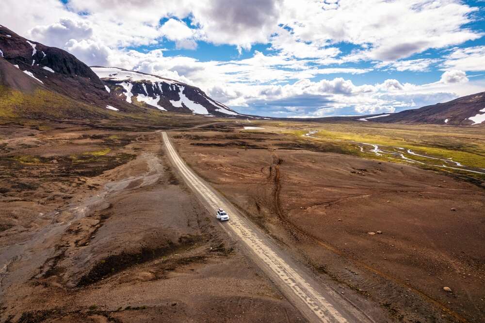 Route isolée traversant une vallée aride et montagneuse en Islande, avec un 4x4 roulant au milieu de ce paysage sauvage.