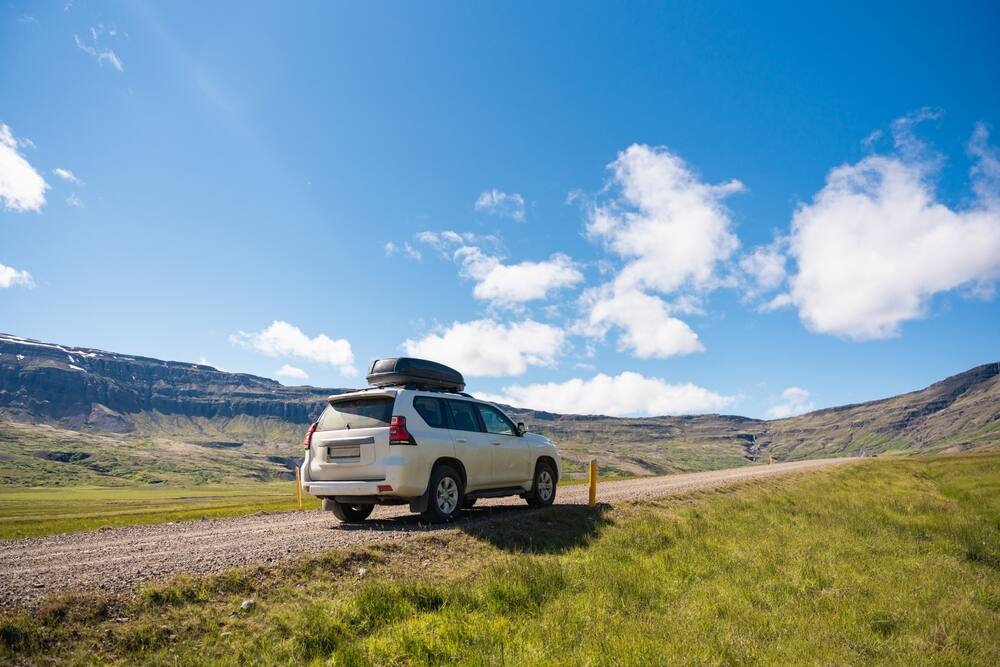 Un SUV blanc garé sur une route de gravier au milieu des montagnes islandaises sous un ciel bleu dégagé.
