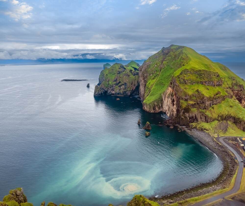 Vue aérienne des îles Vestmann en Islande, présentant des falaises verdoyantes entourées par l'océan bleu profond.