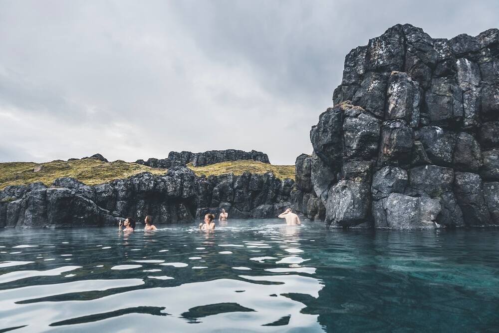 Piscine géothermique naturelle au milieu des roches volcaniques Un groupe de personnes se baignant dans une piscine naturelle entourée de formations rocheuses volcaniques sombres.