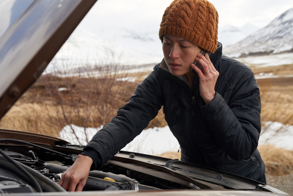 Panne en Islande : que faire en cas de problème mécanique en pleine nature ? Femme en bonnet orange appelant de l’aide au bord de la route en Islande, capot ouvert face à une panne mécanique.
