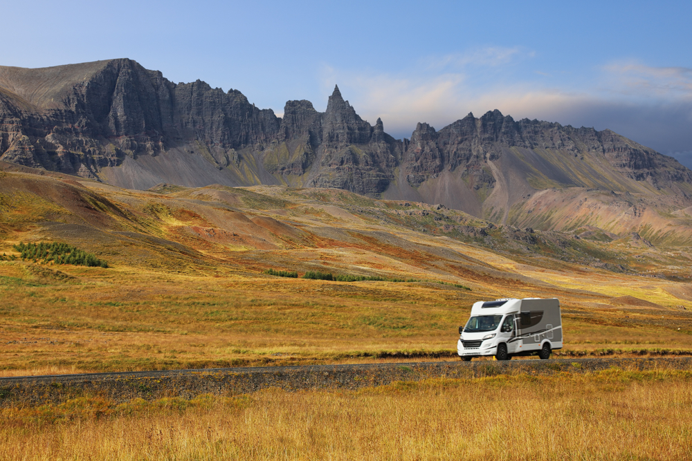 Explorer l’Islande en camping-car : liberté et nature au cœur des terres volcaniques Camping-car roulant à travers les paysages colorés et montagneux d’Islande sous un ciel bleu clair.