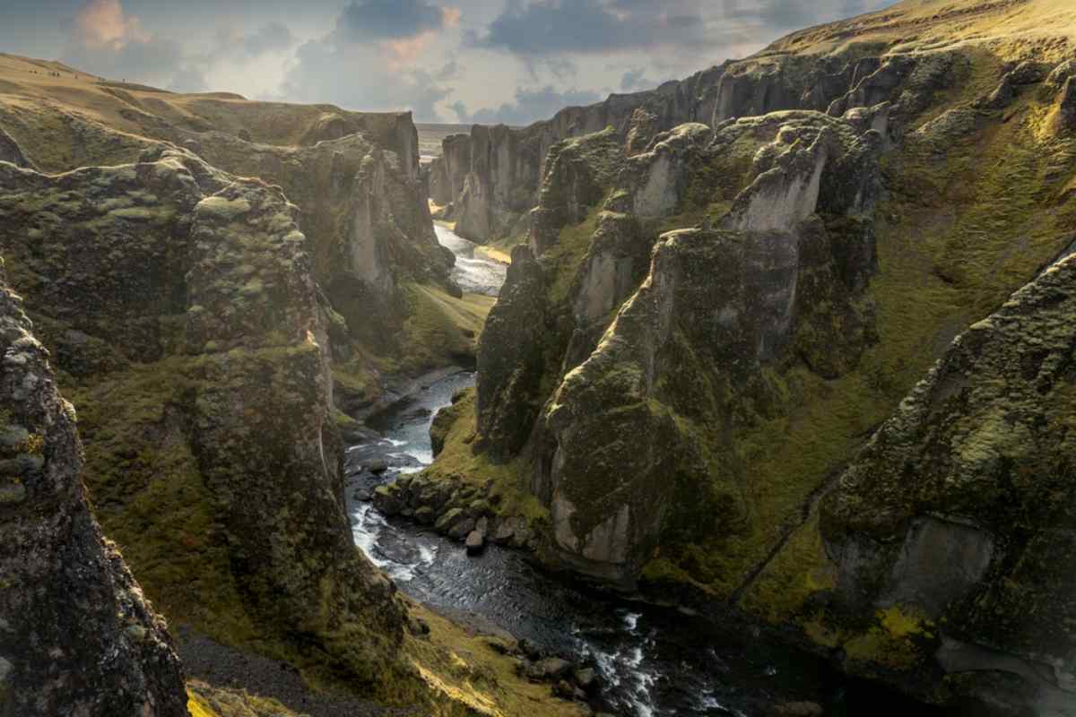 Vue drone du canyon islandais Fjaðrárgljúfur avec une rivière tumultueuse entre des montagnes spectaculaires.