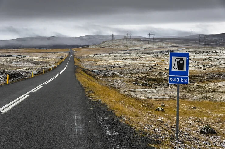 Strada deserta in Islanda con un cartello che segnala la prossima stazione di servizio a 243 km di distanza.