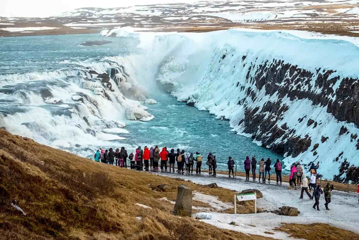 Visitatori osservano la spettacolare cascata Gullfoss immersa in un paesaggio invernale islandese.
