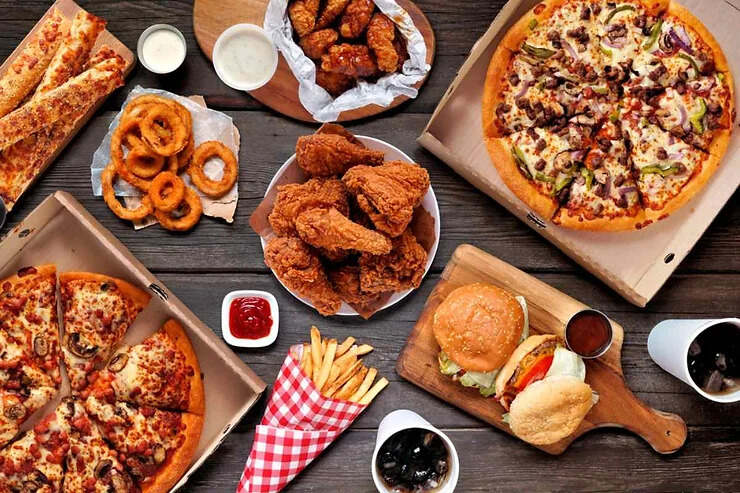 Una varietà di cibi fast food come pollo fritto, anelli di cipolla, patatine fritte e pizze.
