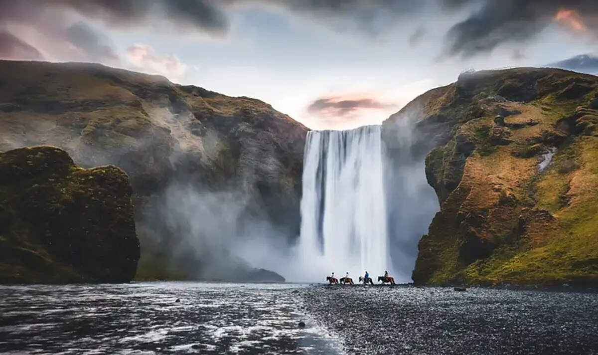 Skógafoss Cascata imponente con cavalli al galoppo, circondata da montagne verdi e un cielo nuvoloso, simbolo delle meraviglie naturali dell'Islanda.