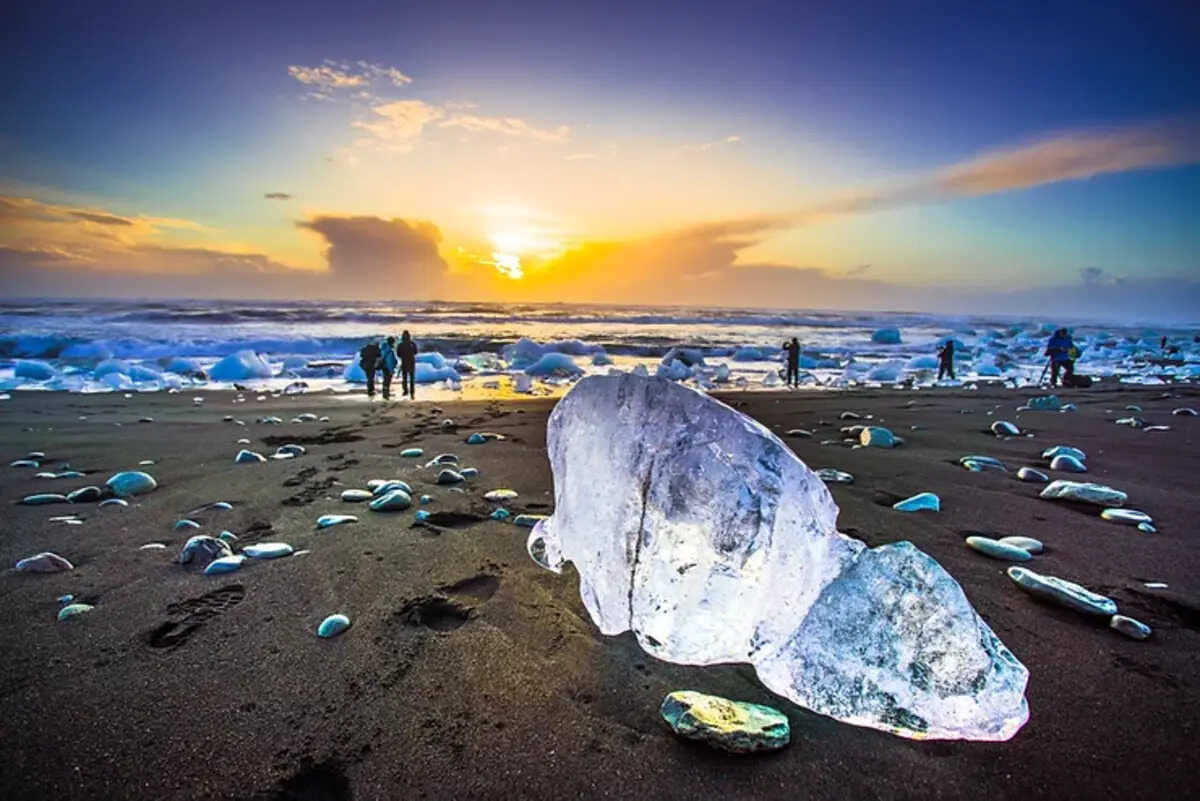 Diamond Beach Ghiaccio scintillante su una spiaggia nera all'alba, con persone che esplorano il paesaggio surreale della Spiaggia dei Diamanti in Islanda.