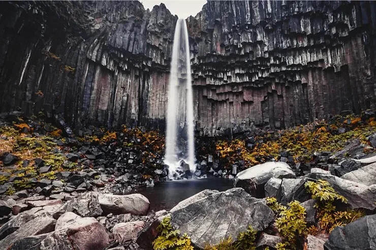 Una cascata famosa situata nel Parco Nazionale di Skaftafell, caratterizzata dalle sue colonne di basalto nero che formano uno sfondo naturale unico. L'acqua scende con eleganza tra le rocce.