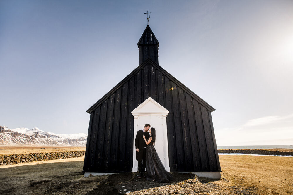 Una coppia davanti alla chiesa nera di Búðir, un luogo iconico dell’Islanda. L’immagine rappresenta semplicità e tradizione in un contesto unico.