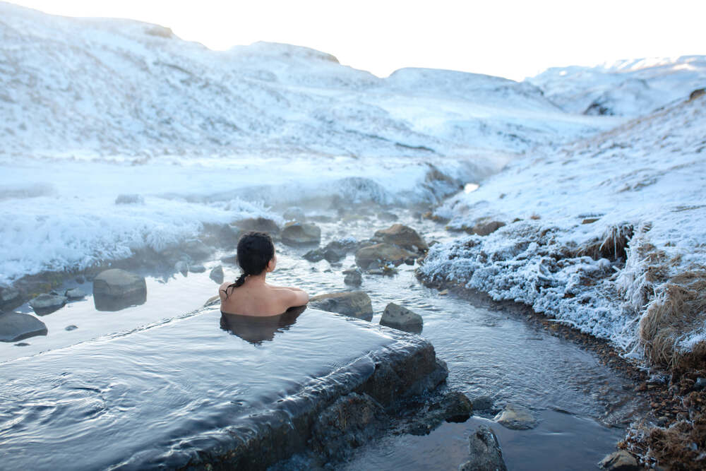 Una persona si rilassa in una sorgente termale naturale, circondata da neve e paesaggi montani innevati.