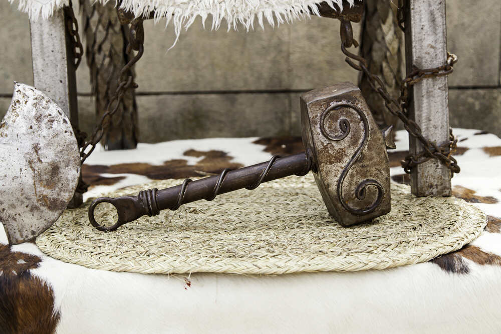 Una riproduzione del Mjölnir, il martello di Thor, in metallo con dettagli intarsiati, appoggiato su una base di paglia accanto ad altri elementi decorativi in stile nordico.