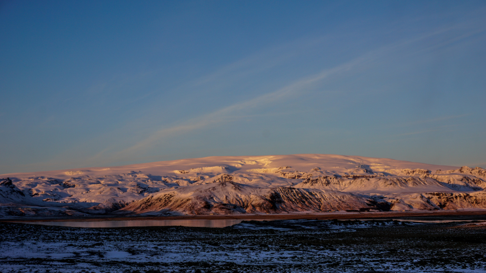 Snow-covered Katla volcano in Iceland glowing under soft sunrise light, with frozen terrain and serene skies marking its icy slumber.