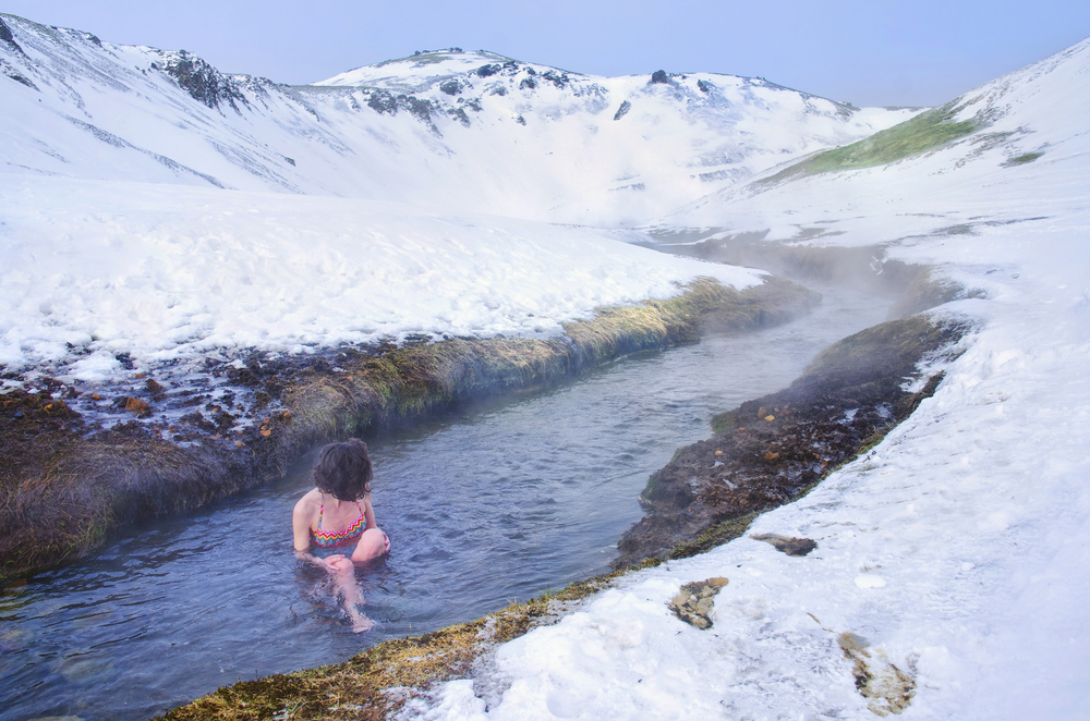 Bagno Termale Invernale a Reykadalur: Relax tra Neve e Vapore in Islanda Donna che si rilassa nel fiume caldo di Reykadalur, Islanda, circondata da neve e vapore termale in un paesaggio invernale mozzafiato.
