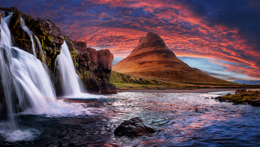 Montagna Kirkjufell al tramonto con la cascata Kirkjufellsfoss in primo piano, Islanda, sotto un cielo spettacolare dai colori intensi.