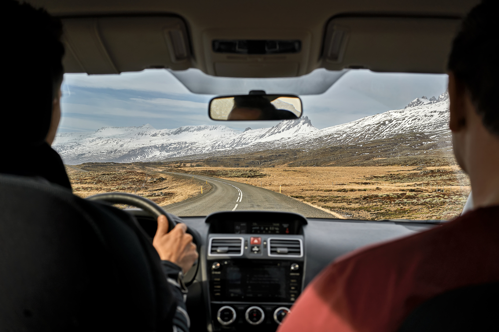Due persone in auto durante un road trip in Islanda con vista panoramica su strade e montagne innevate.