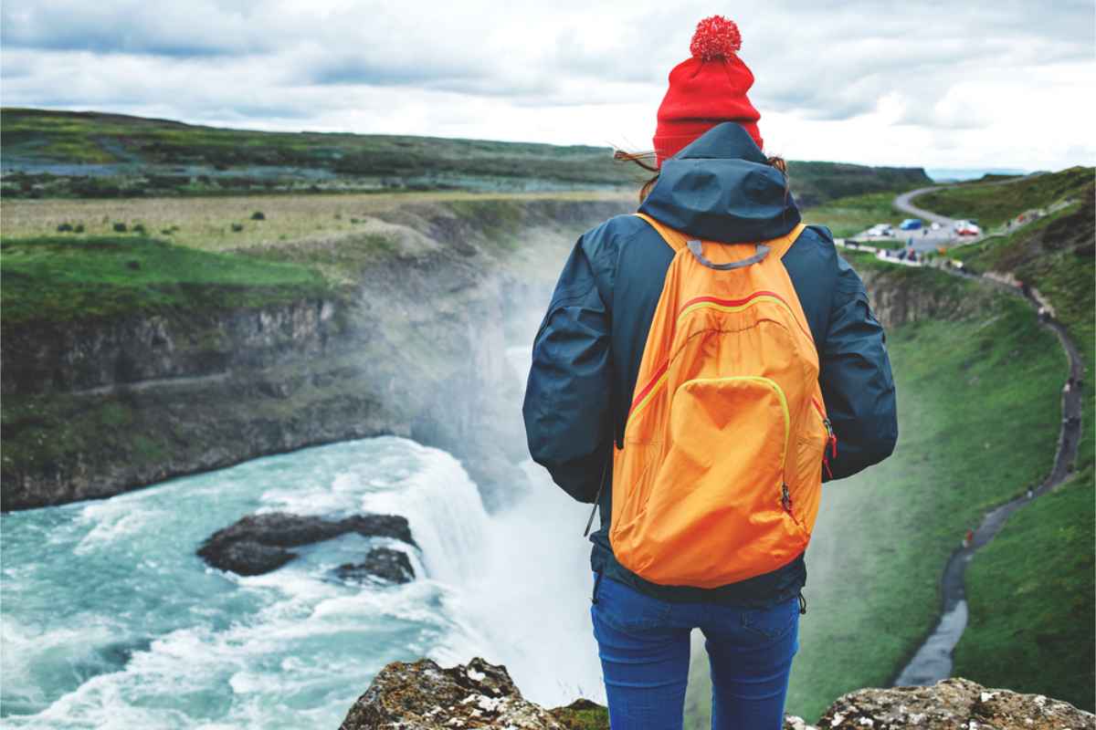 Viaggiatrici solitarie che si godono le cascate islandesi indossando uno zaino arancione brillante