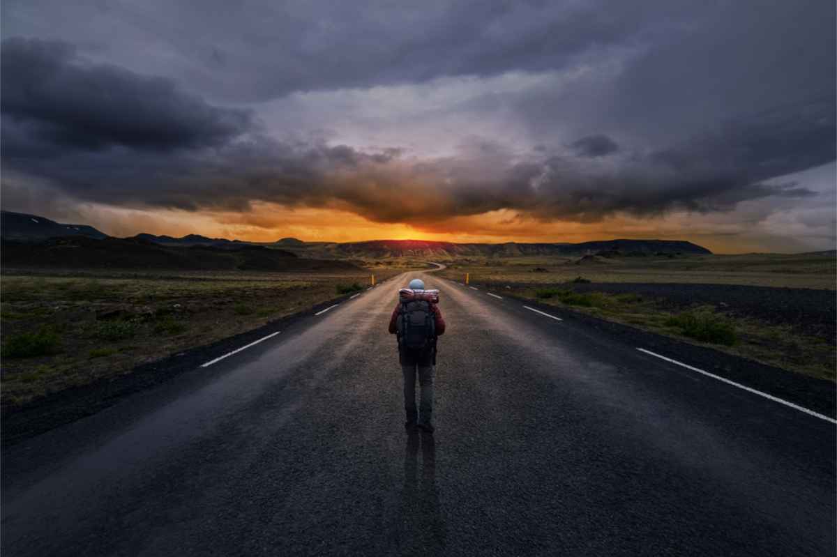 Viaggiatore solitario con lo zaino che cammina lungo una strada deserta in Islanda